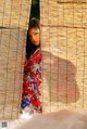 A woman in a red kimono standing in front of a bamboo wall.