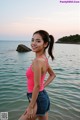 A woman in a pink tank top and denim shorts standing in the water.