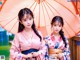 Two young women in kimonos standing under an umbrella.