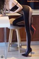 A woman in a black bodysuit and high heels sitting at a table.