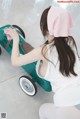 A woman in a white shirt and a pink headband cleaning a green toy car.