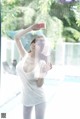 A woman in a white tank top is spraying water on her face.