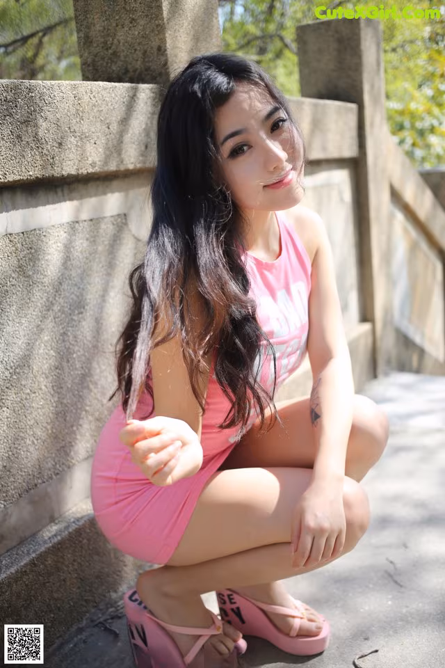 A woman in a pink dress sitting on a stone wall.