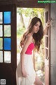 A woman in a pink top and white skirt leaning against a door.