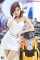 A woman in a white dress standing next to a motorcycle.