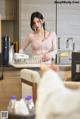 A woman in a pink shirt is washing dishes in a kitchen.