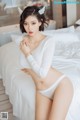 A woman in a white sweater and panties sitting on a bed.