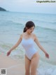 A woman in a white bathing suit walking on the beach.