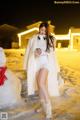 A woman standing next to a snowman in the snow.