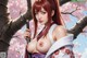 A woman with red hair holds a sword under cherry blossoms.