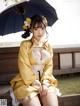 A woman in a yellow kimono sitting on a bench holding an umbrella.