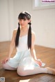 A young woman sitting on the floor in a white dress.