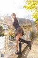 A woman in a school uniform leaning against a fence.