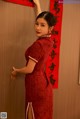 A woman in a red cheongsam leaning against a wall.