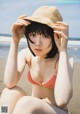 A woman in a bikini and hat sitting on the beach.