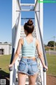 A woman in a blue tank top and denim shorts is walking up some stairs.