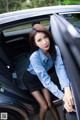 A woman in a blue shirt and black skirt leaning out of a car.