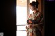 A woman in a kimono holding a fan in front of a window.