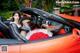 A woman sitting in the driver's seat of a red sports car.