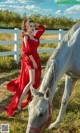 A woman in a red dress standing next to a white horse.