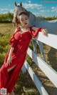 A woman in a red dress leaning against a white fence.